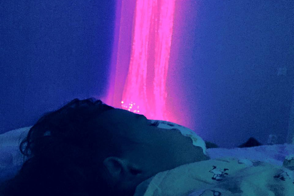 Pojke sover i mörkt rum och på väggen hänger fiberoptik som lyser