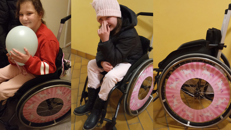 Lycklig flicka i en rullstol med rosa ekerskydd med Unicorns på. 