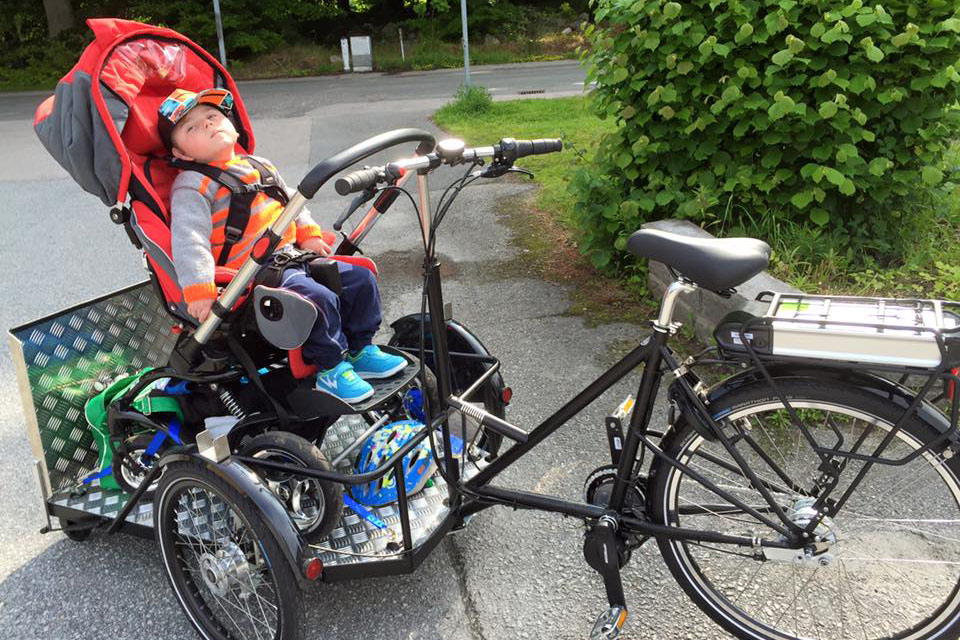 Cykel med flak på vilken det står en rullstol med en pojke