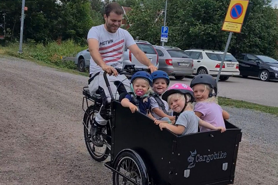 En man cyklar på en lådcykel där fyra glada barn sitter
