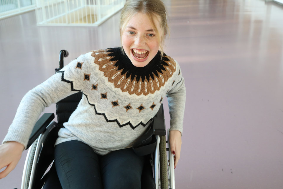 Skrattande tonårsflicka som kör rullstol